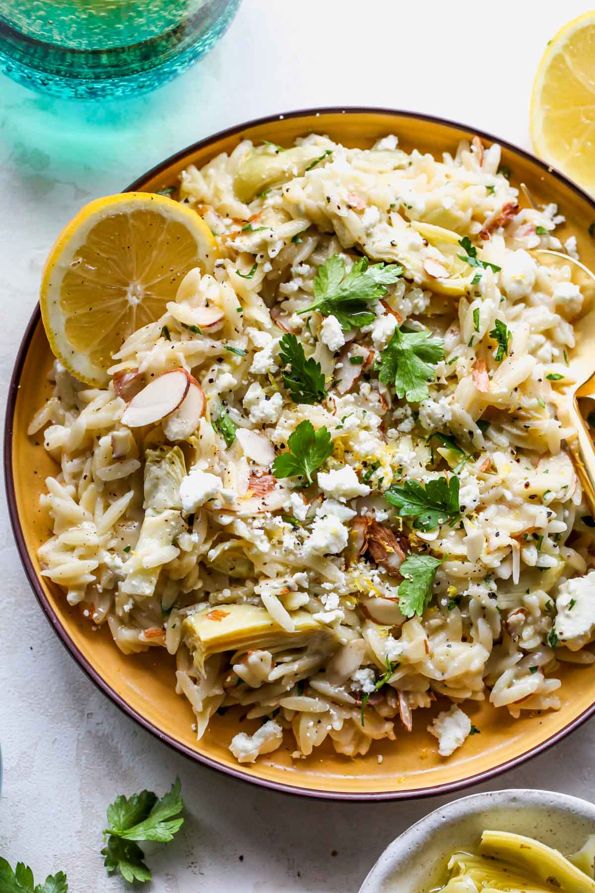 Lemon orzo salad topped with parsley on a plate with a fork and spoon.