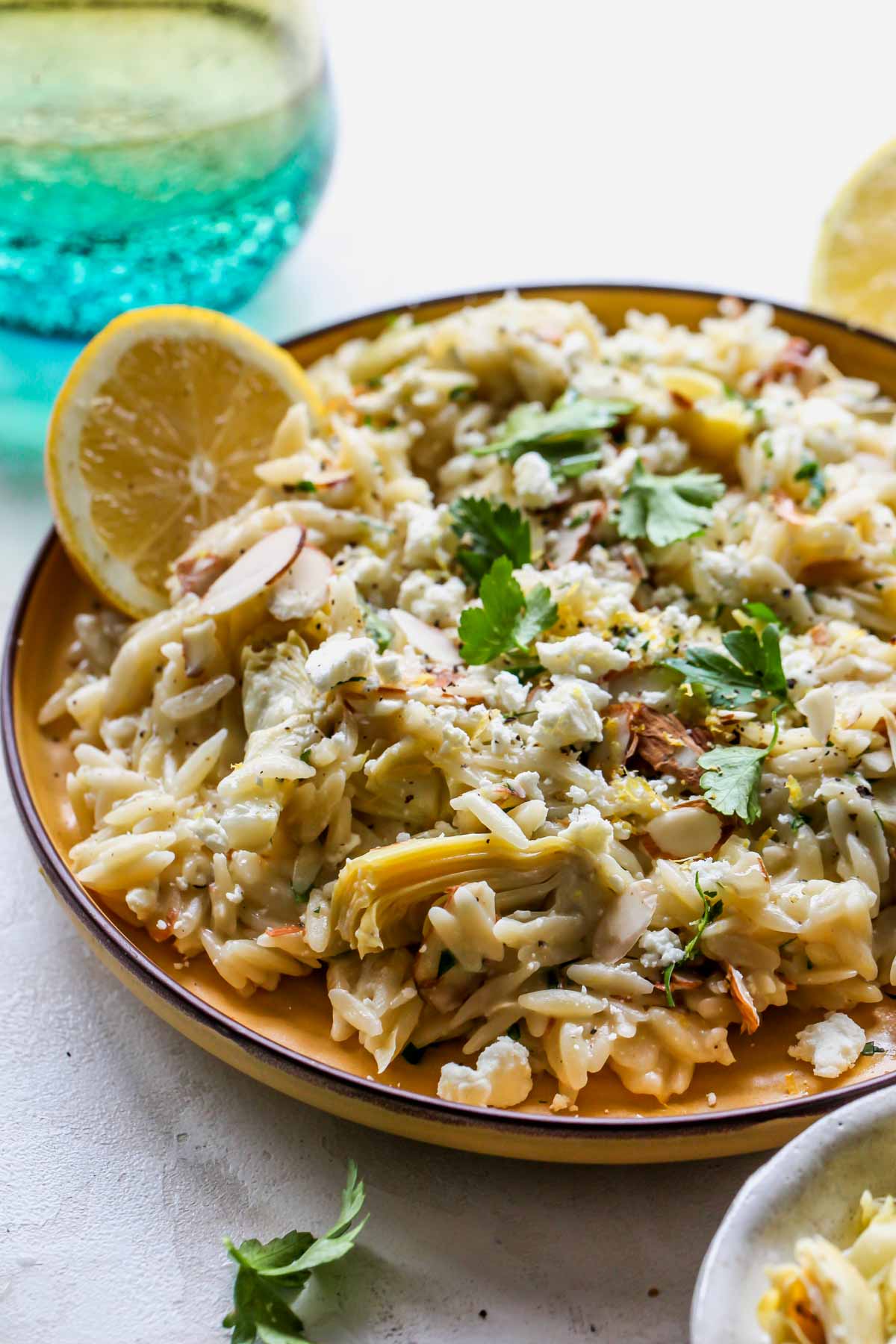 Serving of orzo and veggies styled on a yellow plate