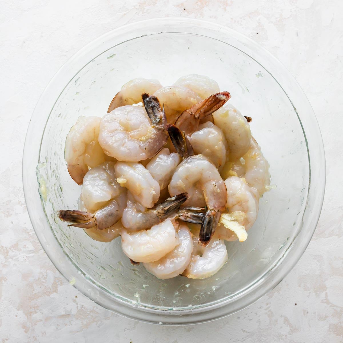 Shrimp being marinated in olive oil and garlic in a bowl