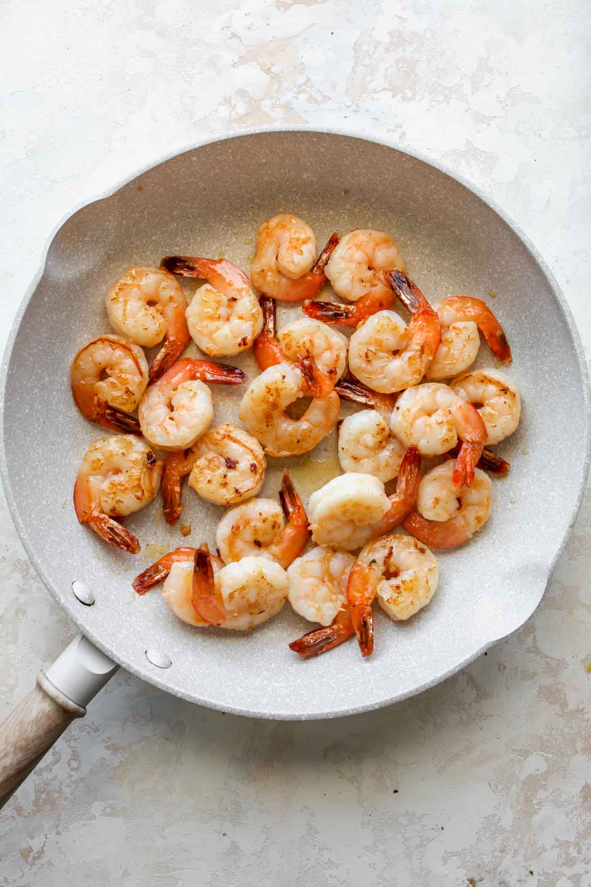 Shrimp being sauteed in olive oil in a white skillet