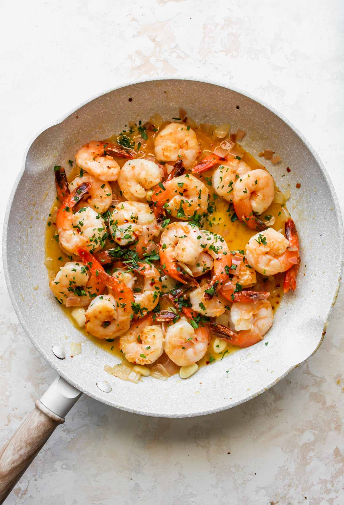 Shrimp and parsley being added to skillet of garlic-butter sauce