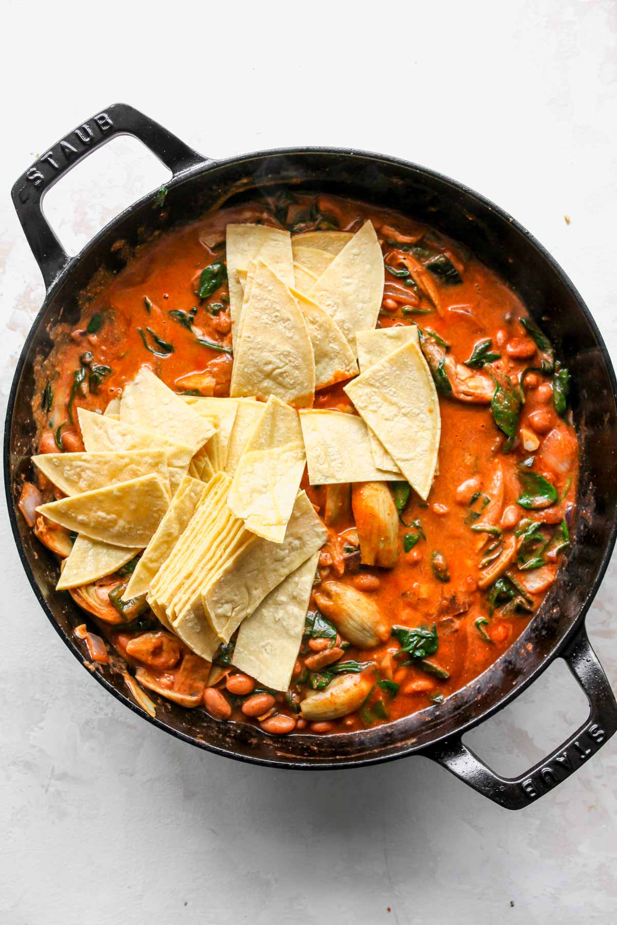 Strips of corn tortillas being mixed into a pan of enchiladas