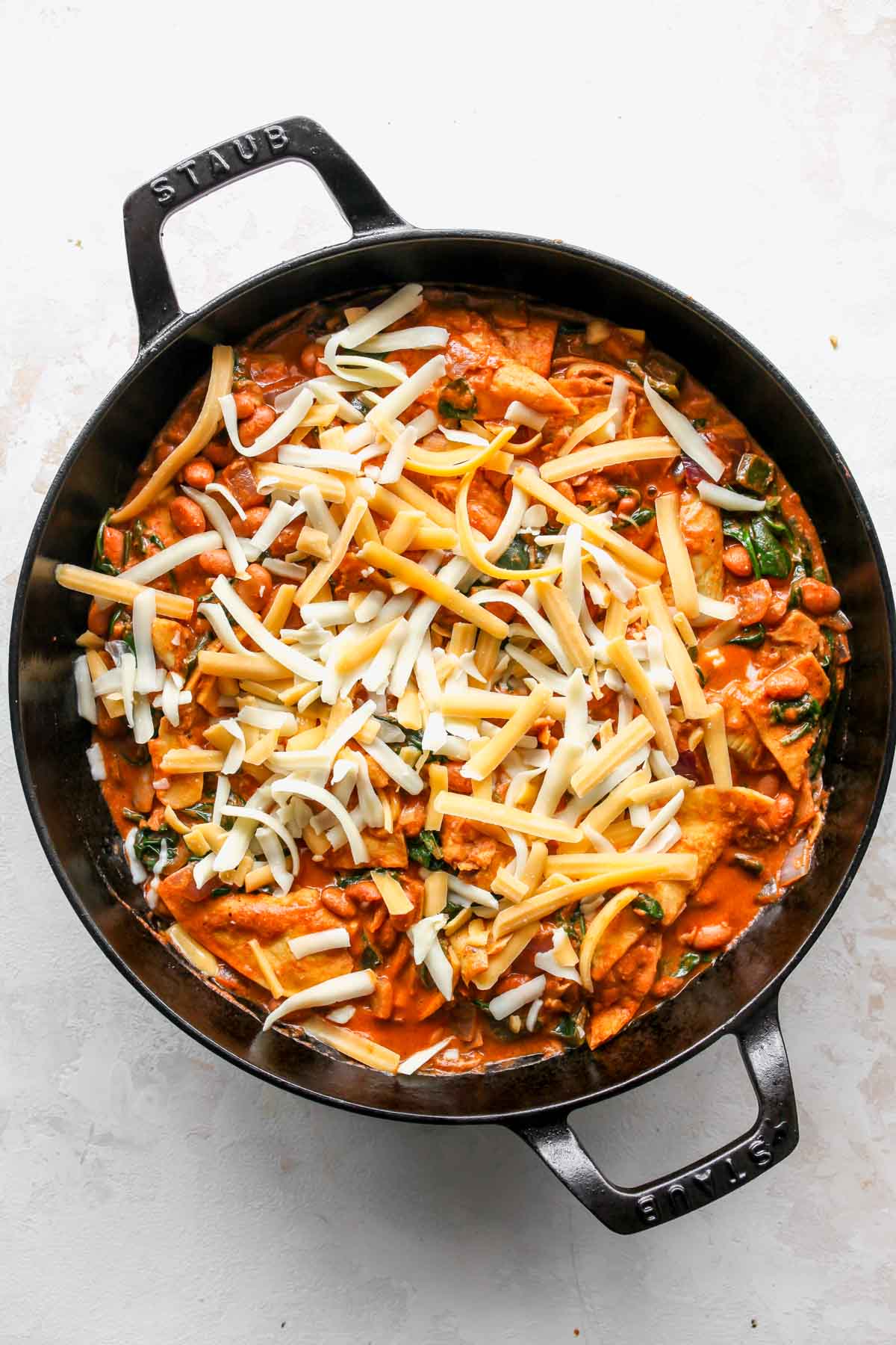 Cheese being sprinkled over a mixture of veggies and enchilada sauce