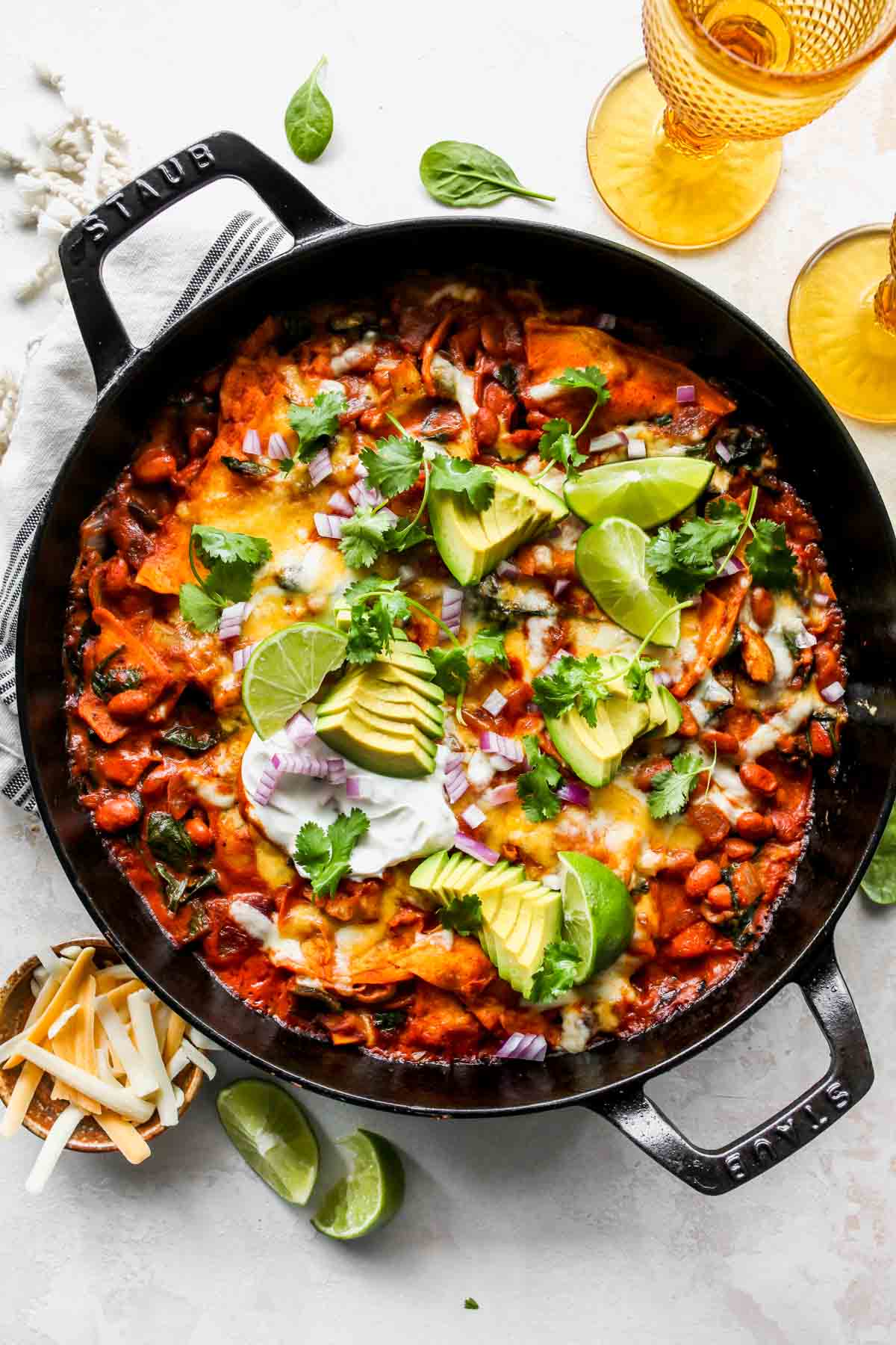 Skillet of vegetable enchiladas topped with avocado slices, cilantro, and lime wedges