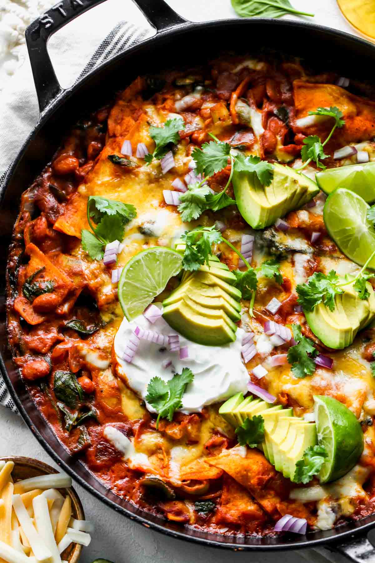Spinach-artichoke skillet enchiladas topped with avocado, lime wedges, and cilantro.