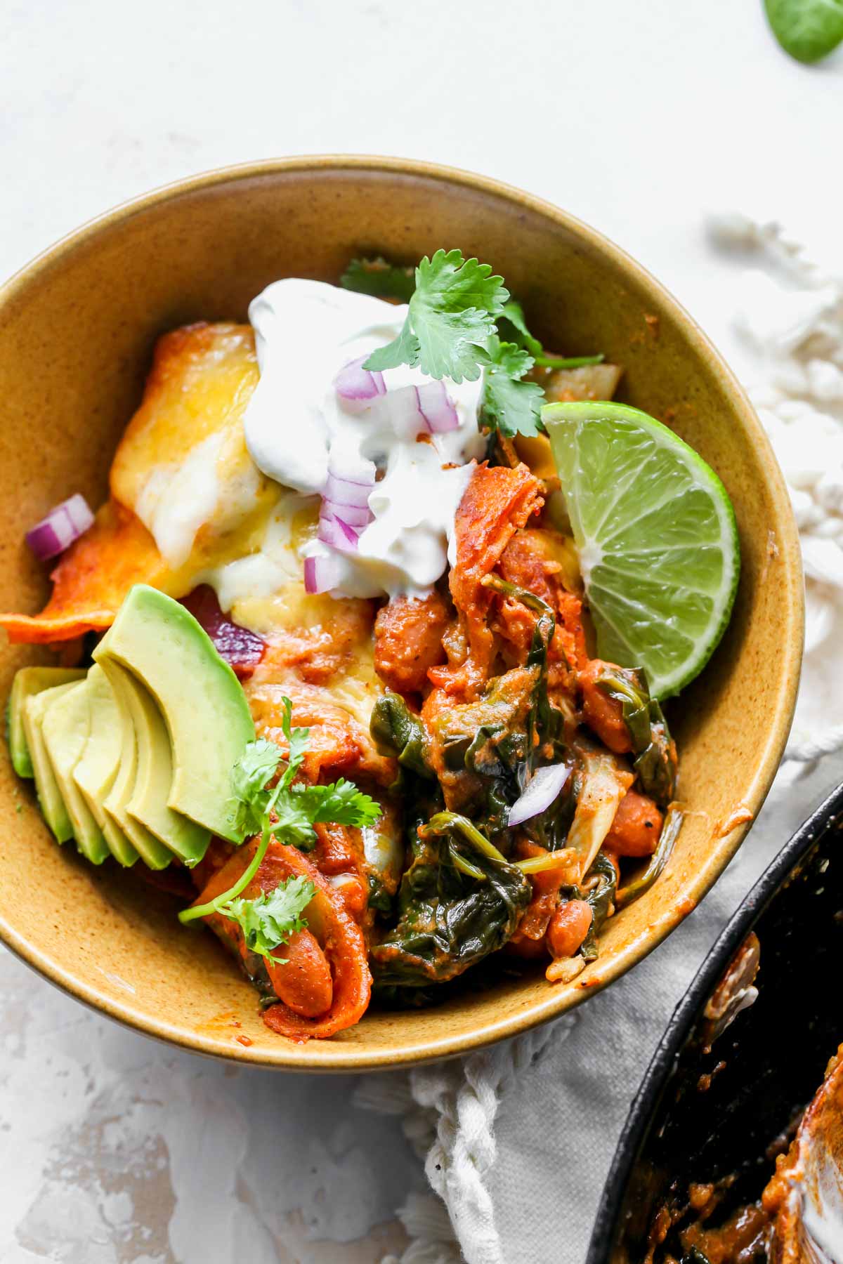 Single serving of spinach and artichoke enchiladas in a gold bowl topped with sour cream and avocado