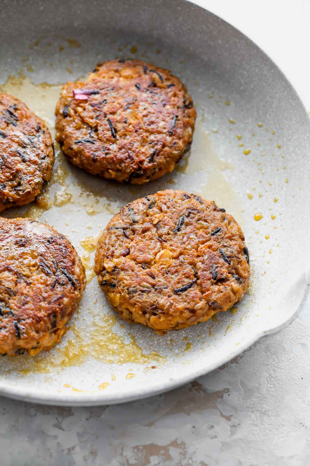 Wild rice veggie burgers being sautéed in a white skillet