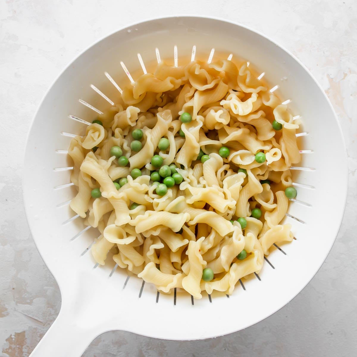 Cooked pasta noodles and green peas in a strainer