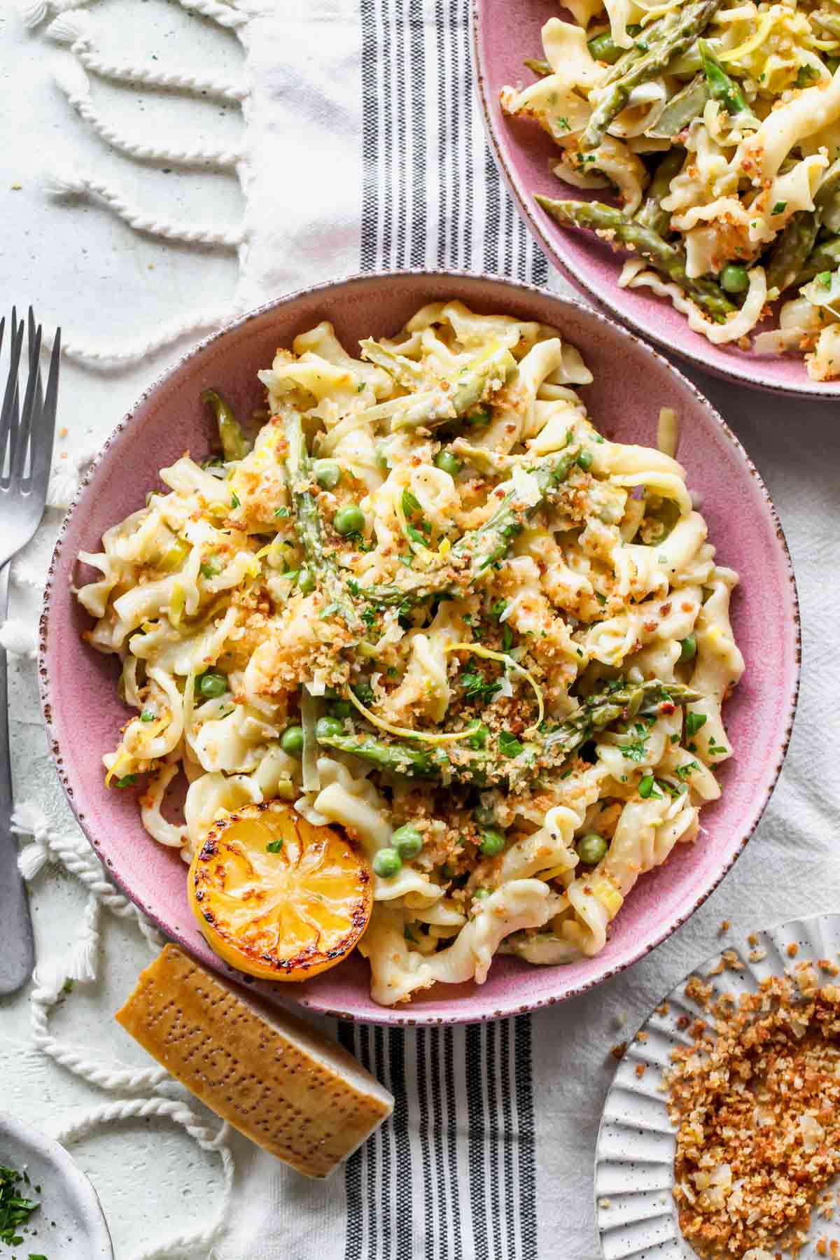 Pasta styled in a pink bowl with asparagus, peas, leeks, and lemon slices