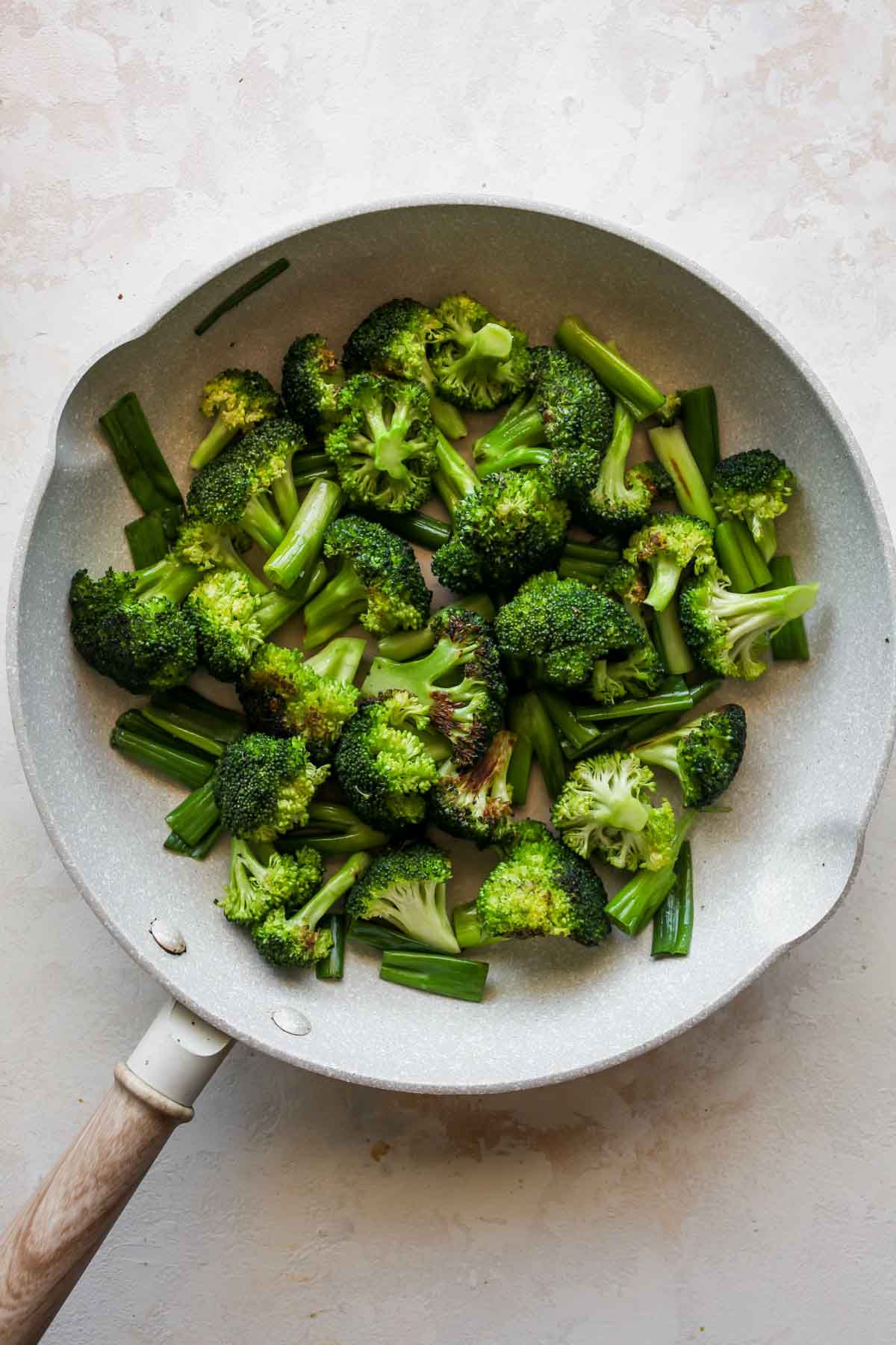 Broccoli florets and green onion being sautéed in a white skillet