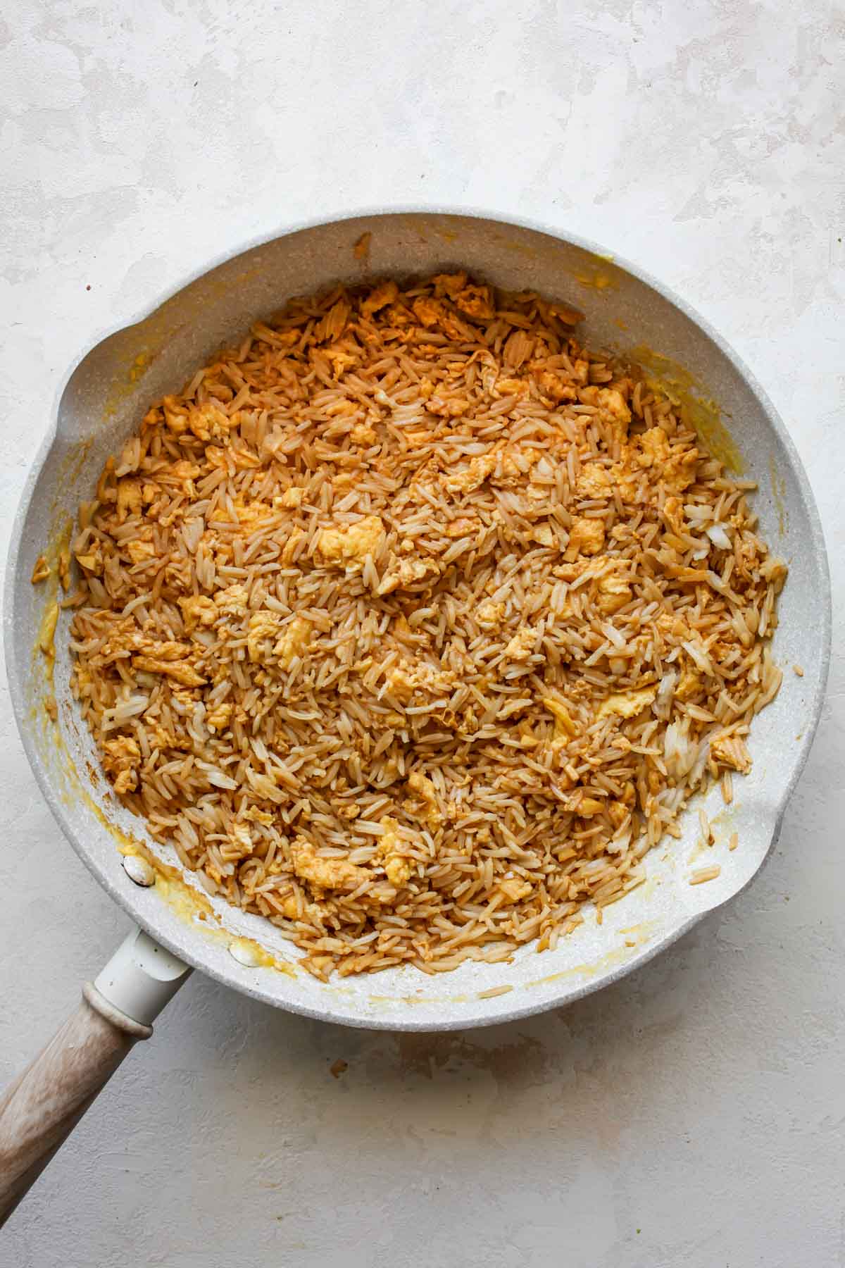 Rice, soy sauce, and eggs cooking in a white skillet