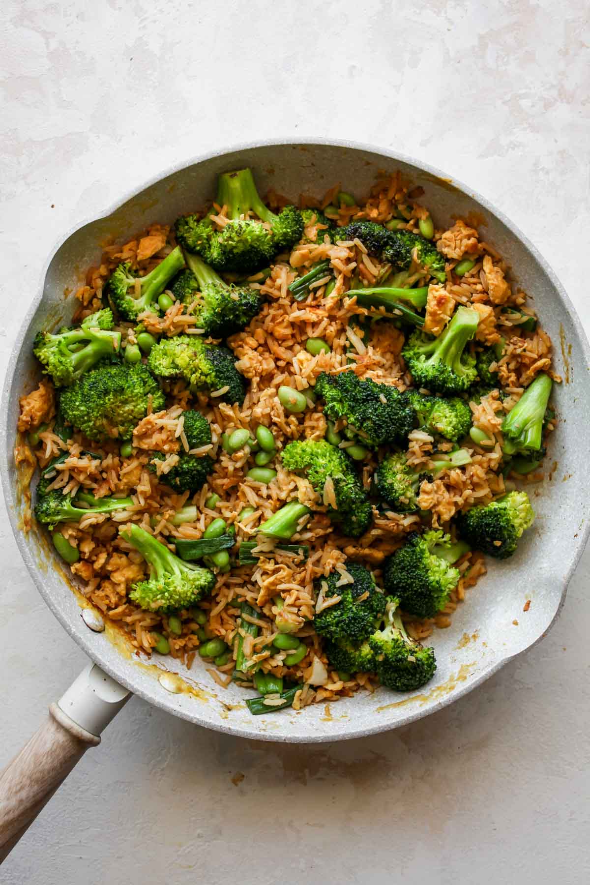 Broccoli, green onion, and edamame being added to skillet with rice