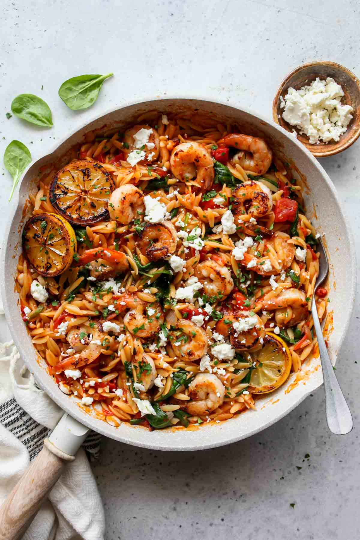 Finished skillet of shrimp orzo in a white skillet topped with fresh parsley and feta