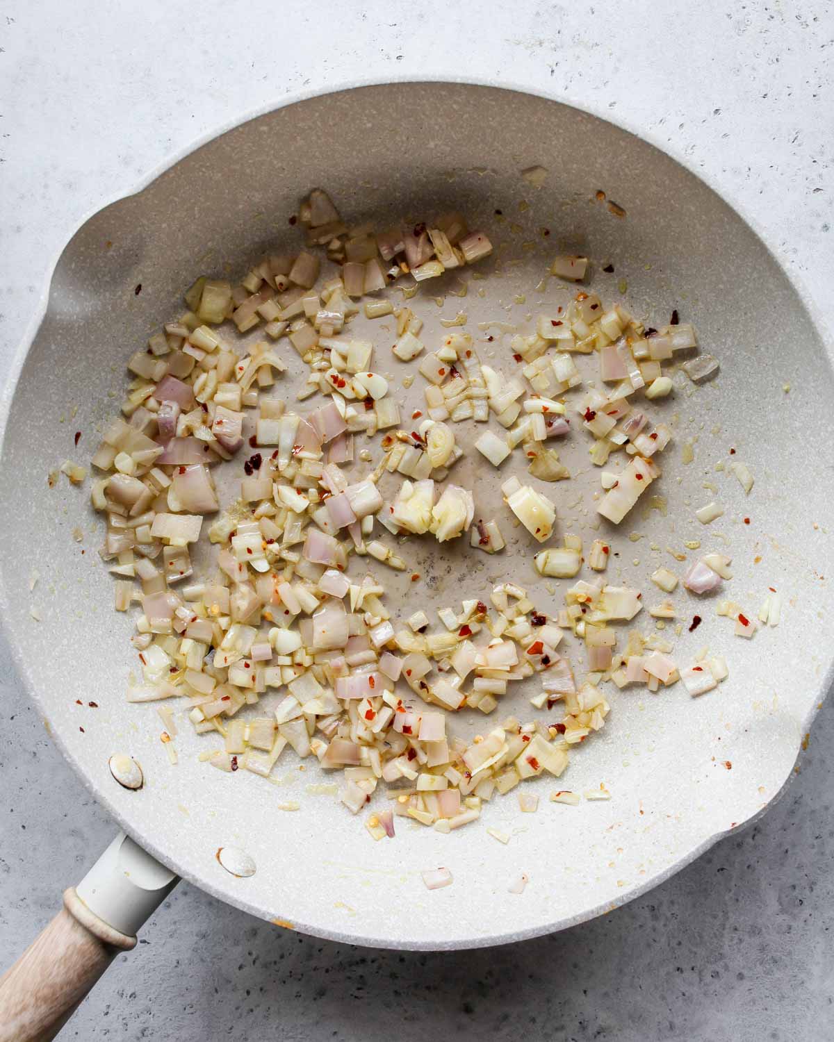 Shallots, garlic, and chili flakes sautéing in a skillet