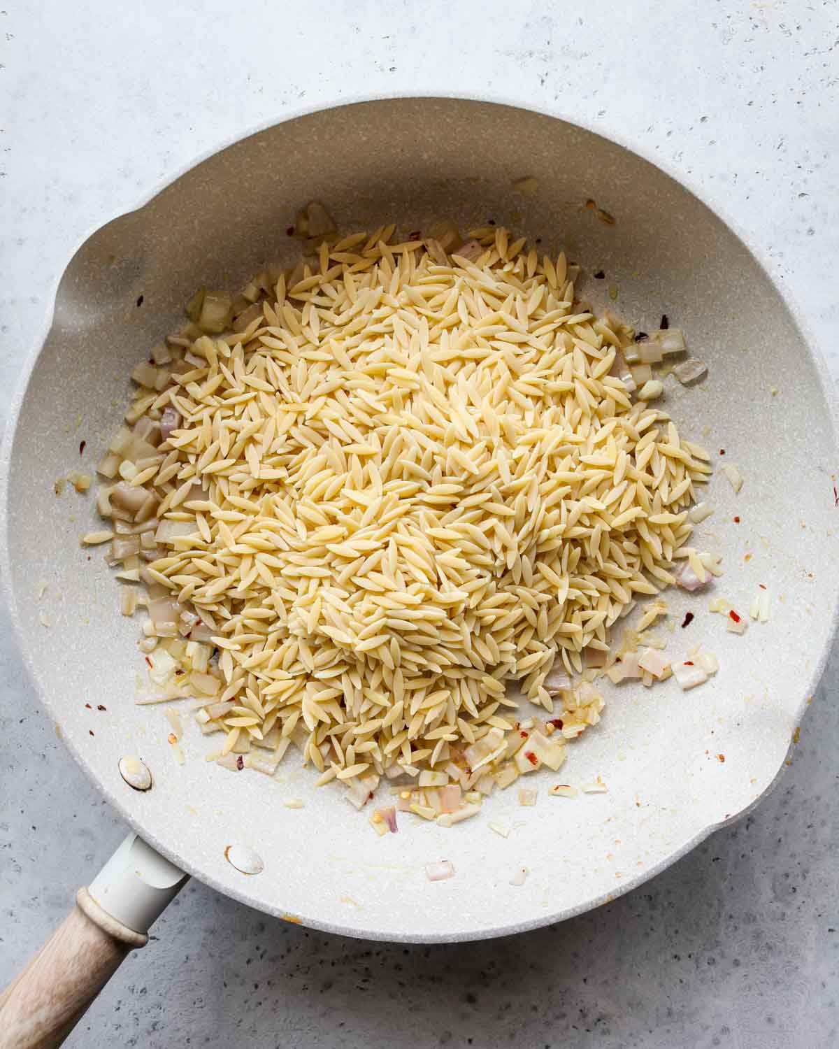 Dry orzo pasta toasting in a white skillet