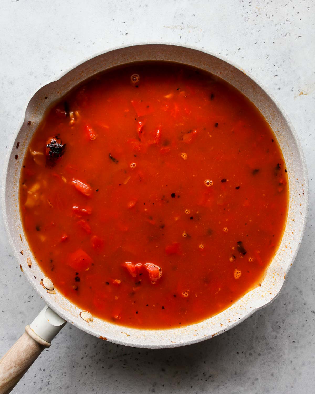Tomatoes and broth being added to orzo mixture in a pan