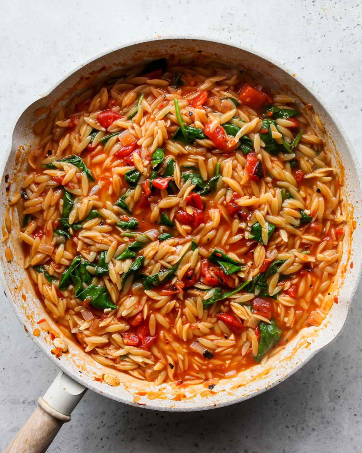 Spinach being mixed into a pan of cooked orzo pasta