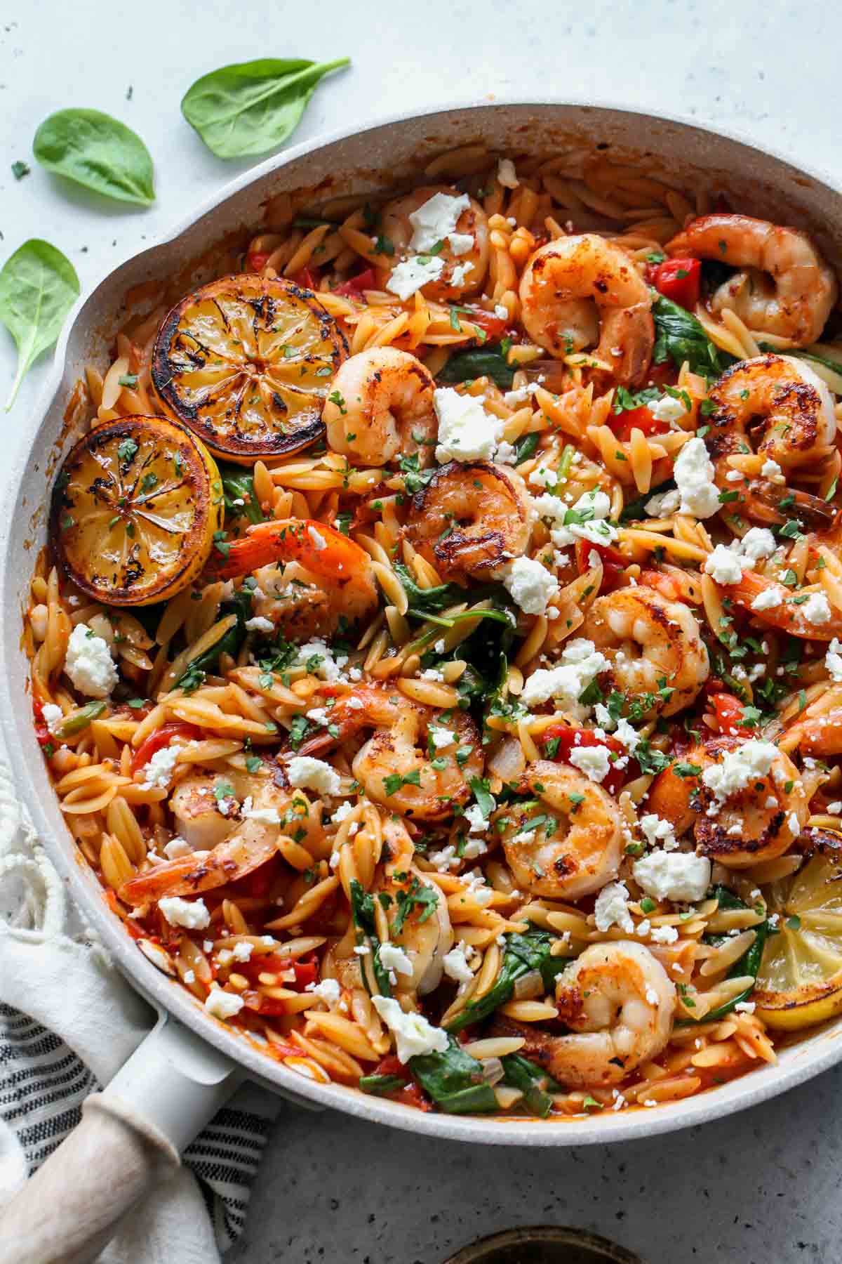 Shrimp and orzo in a white skillet topped with lemon wedges and feta