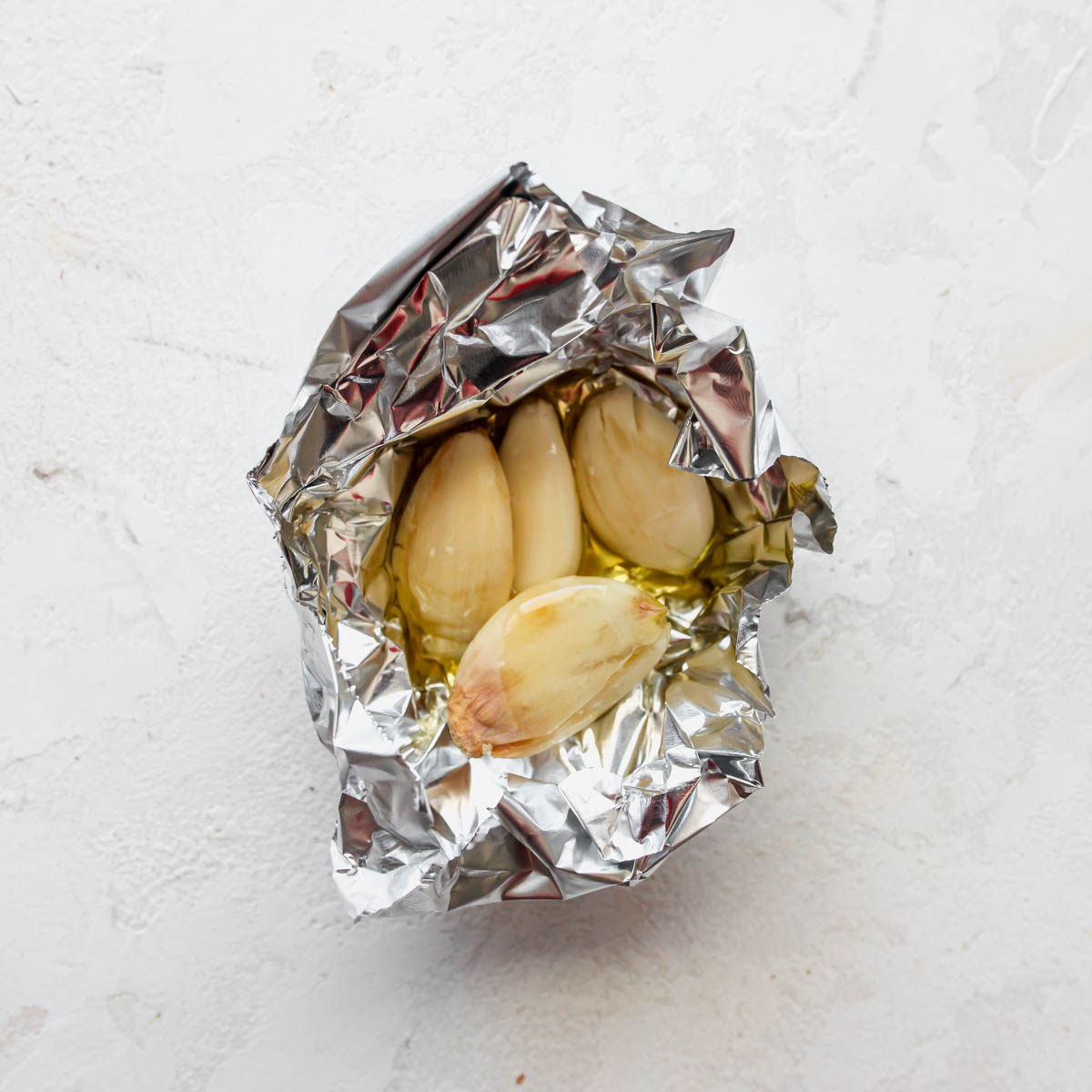 Garlic cloves being coated with oil and wrapped in foil
