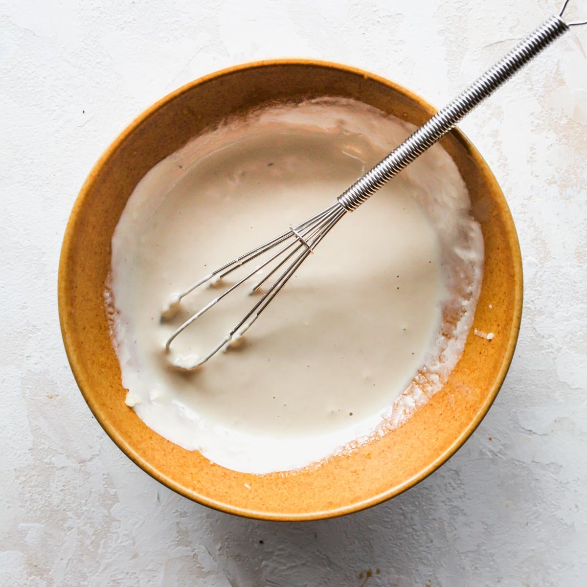 Tahini sauce being whisked in a gold bowl