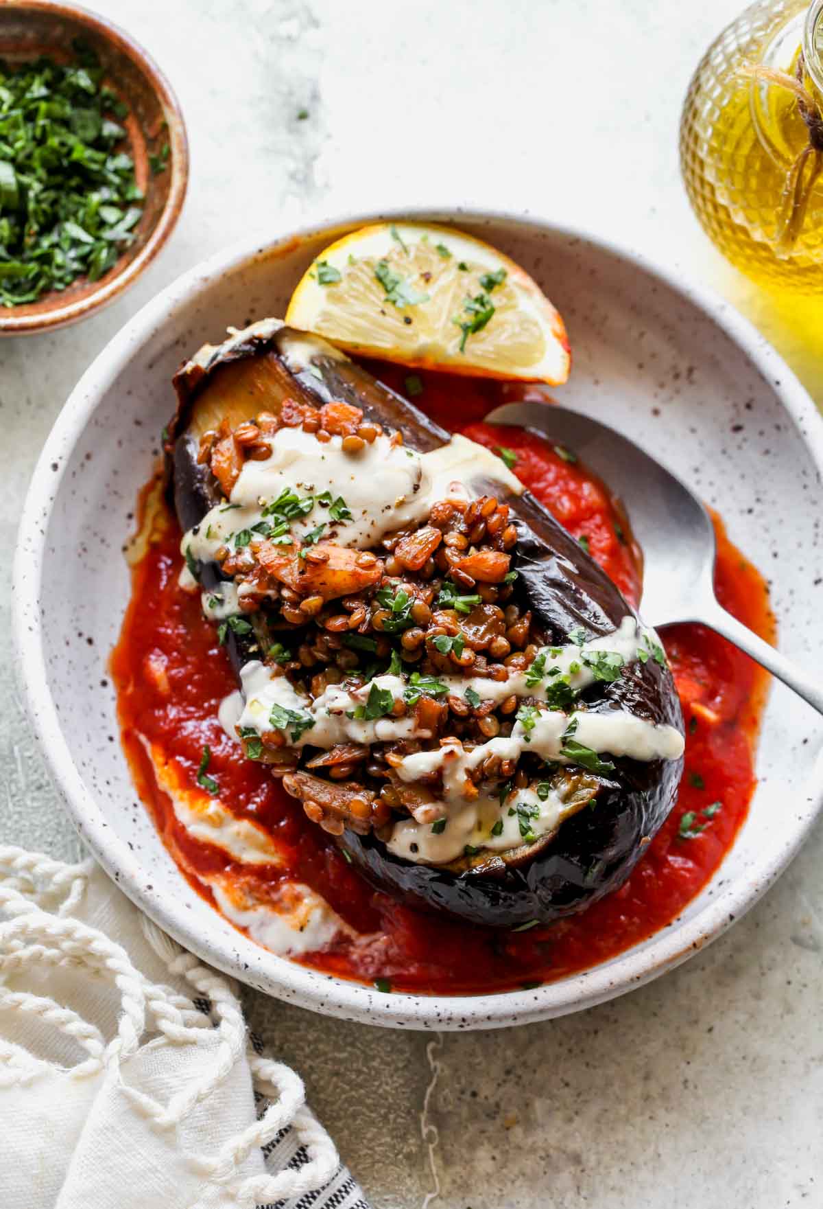 One filled eggplant in a white bowl topped with tahini sauce