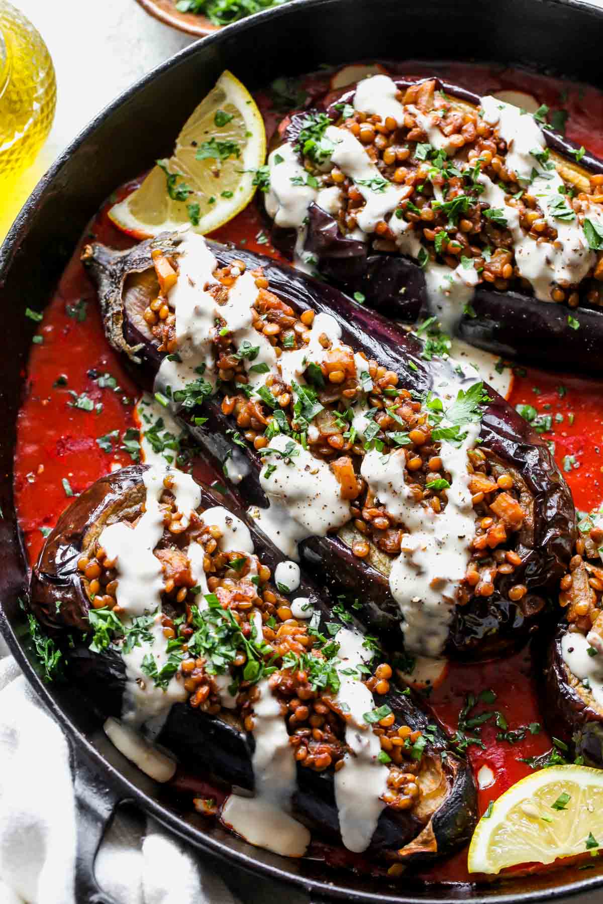 Stuffed eggplants being drizzled with tahini sauce and topped with parsley