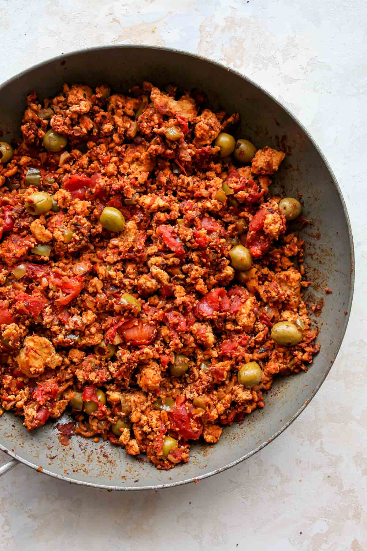Olives and raisins being added to a skillet of vegan picadillo