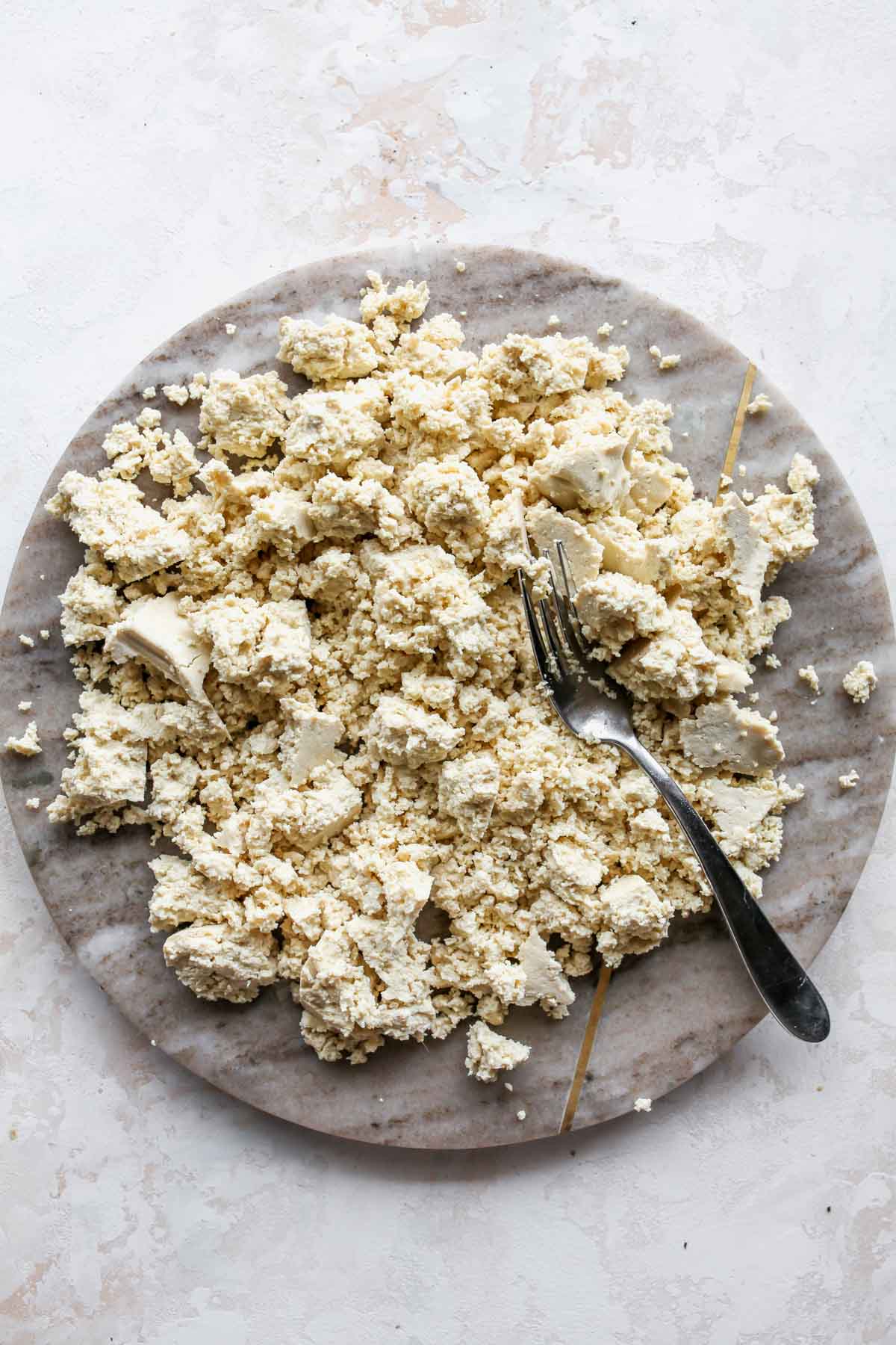 Block of tofu being crumbled into pieces on a cutting board