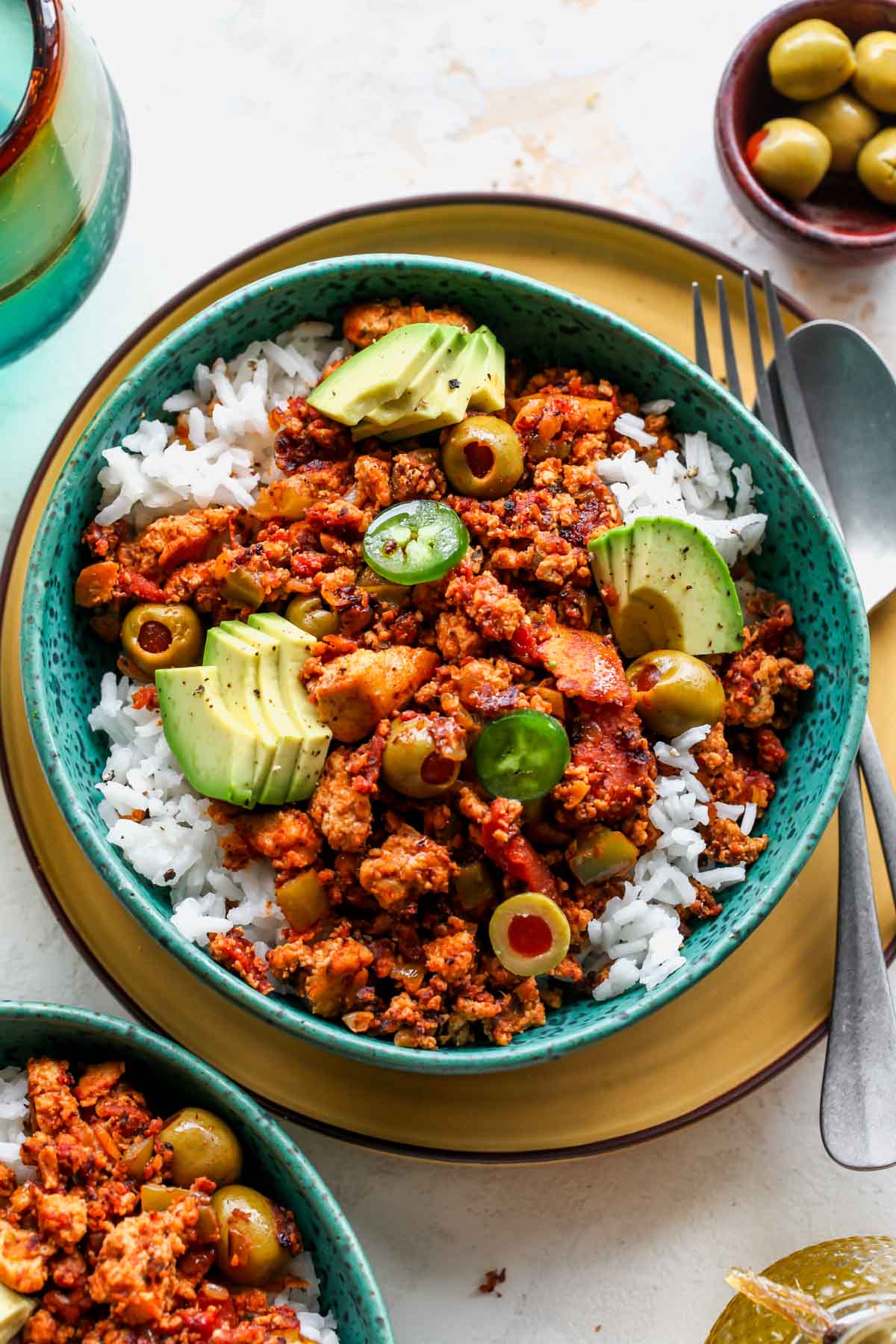 Tofu picadillo served over rice in a teal bowl with avocado slices
