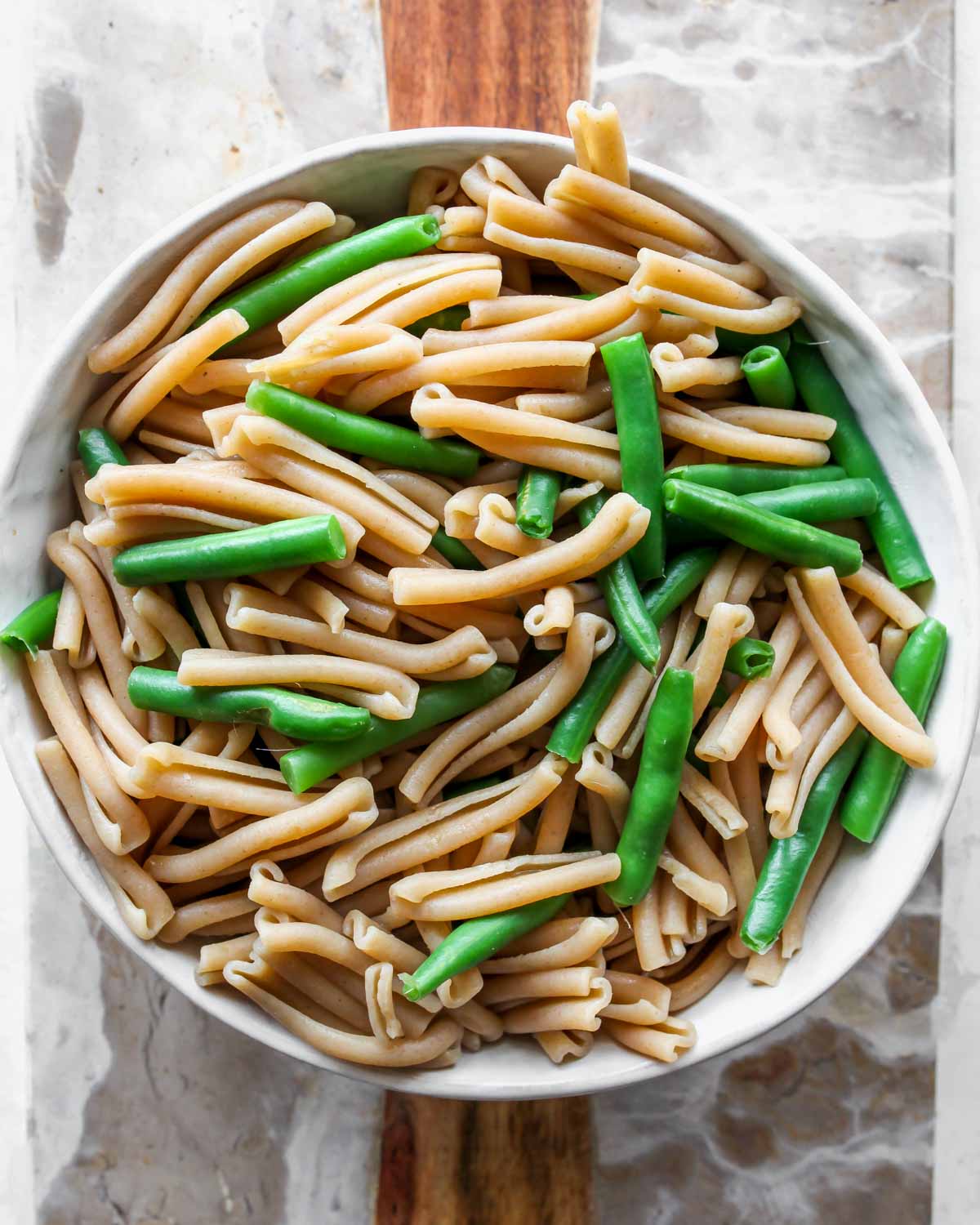 Cooked pasta noodles and green beans draining in a colander
