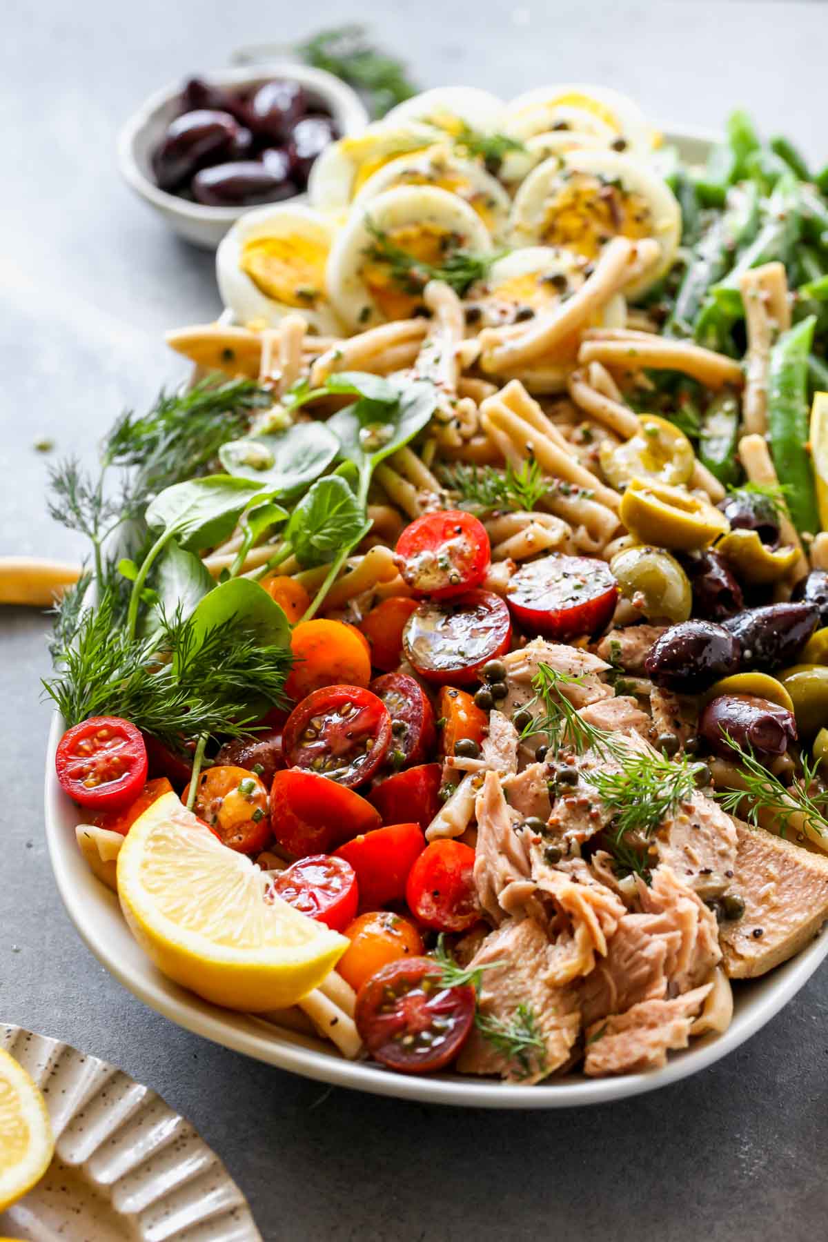 Tuna pasta salad on a platter with tomatoes, eggs, and green beans