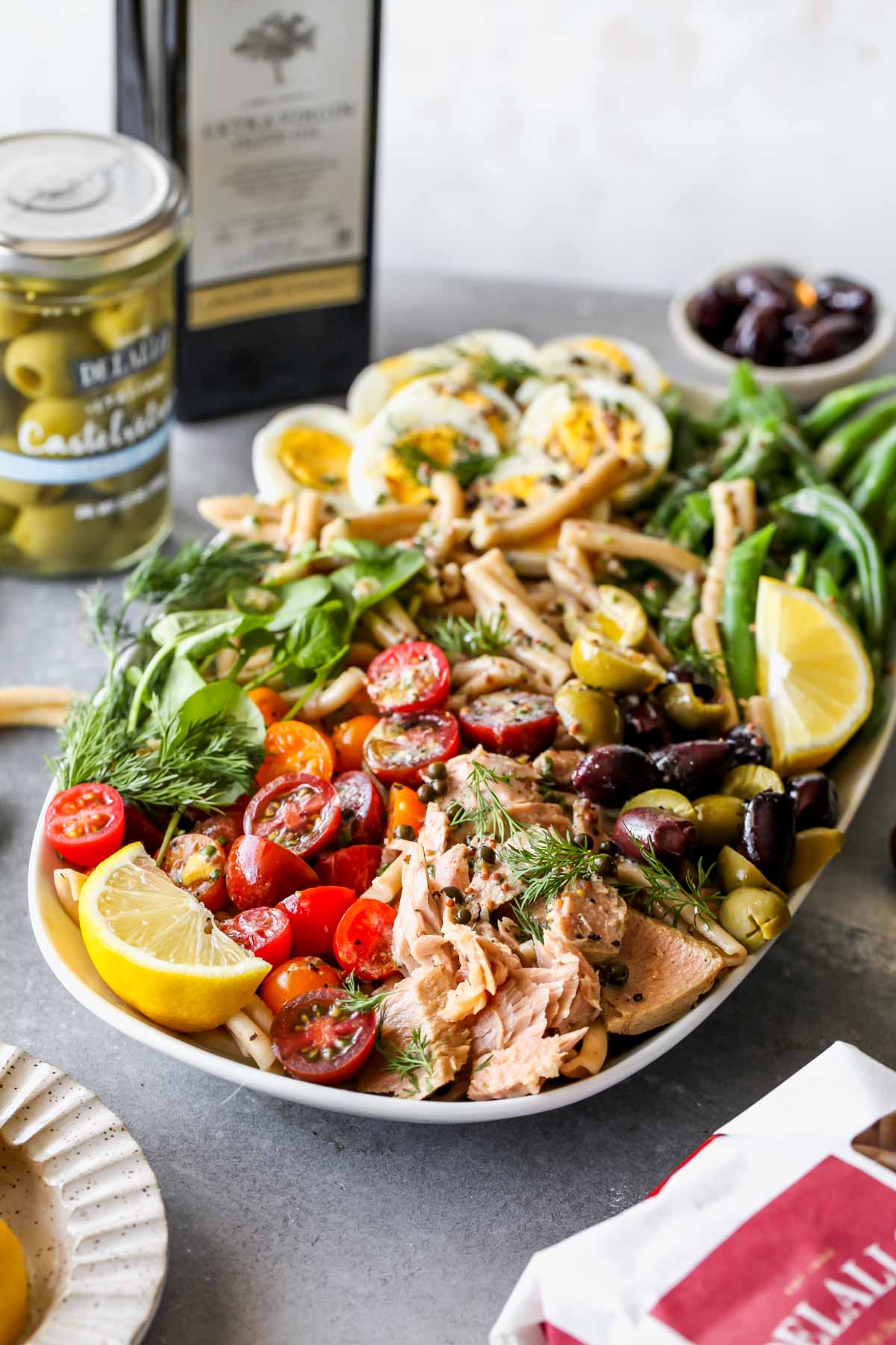 Niçoise Pasta Salad with olive oil and olive jar in the background