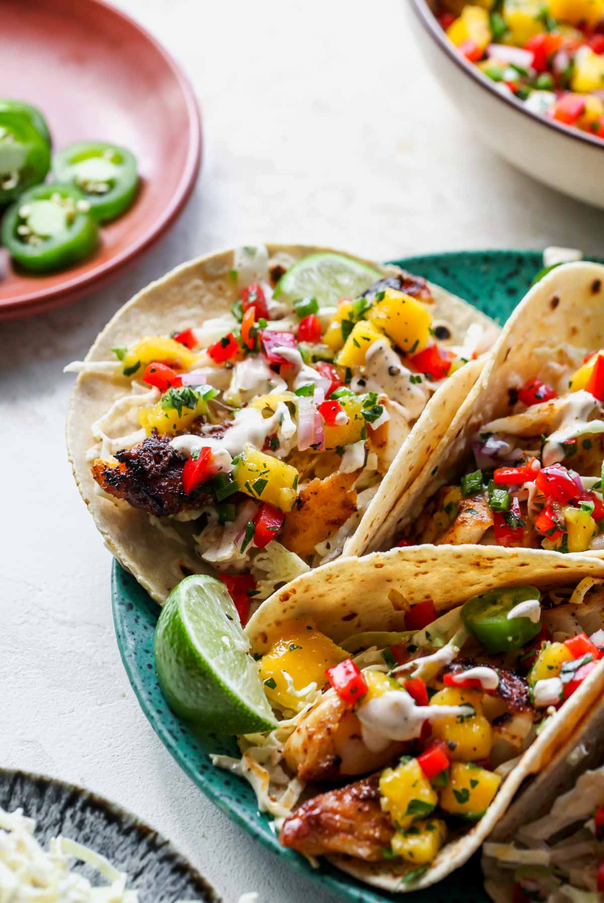 Taco-spiced cod tacos on a plate topped with salsa, slaw, and Baja sauce