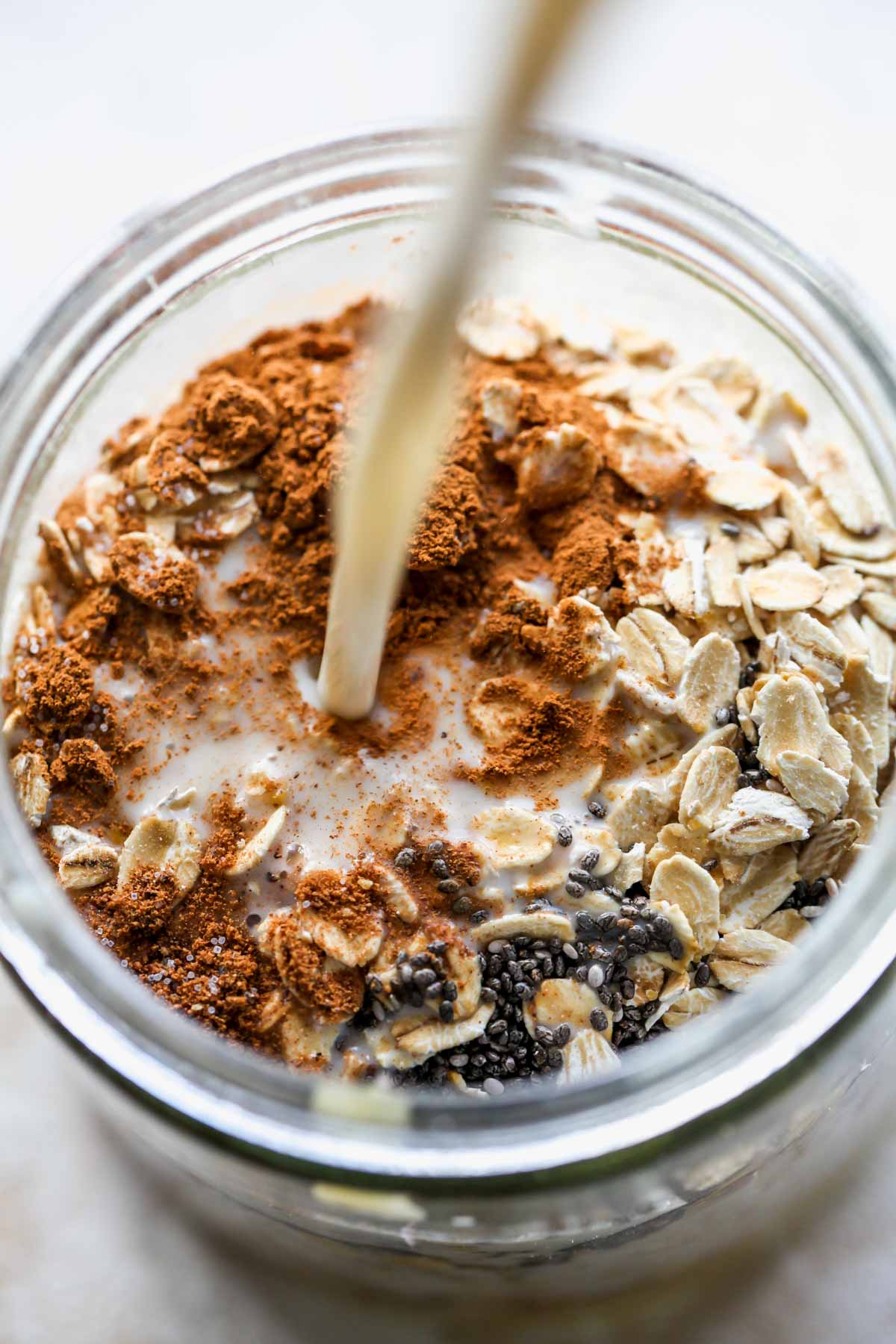 Oatmilk being poured into a jar of rolled oats and chia seeds
