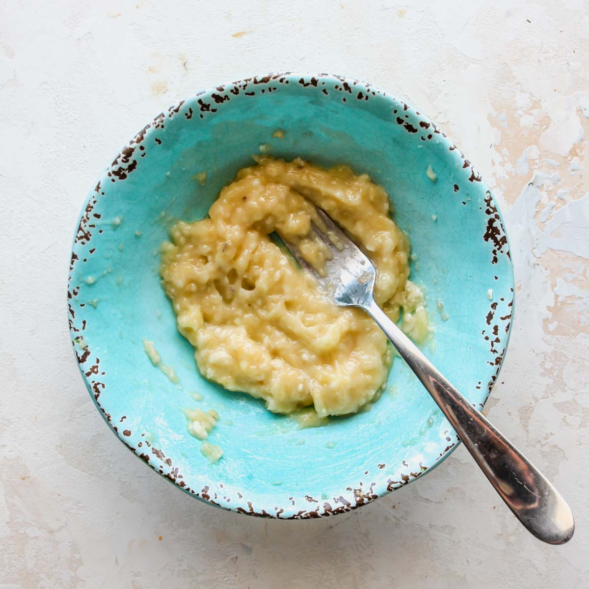 Banana being mashed with a fork in a bowl