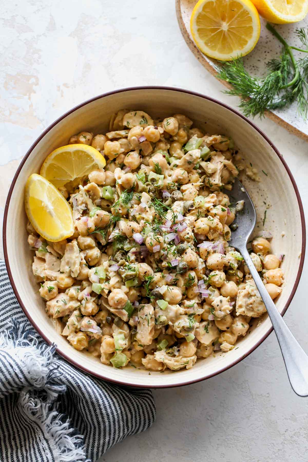 Tuna and chickpea salad in a tan bowl topped with lemon wedges.
