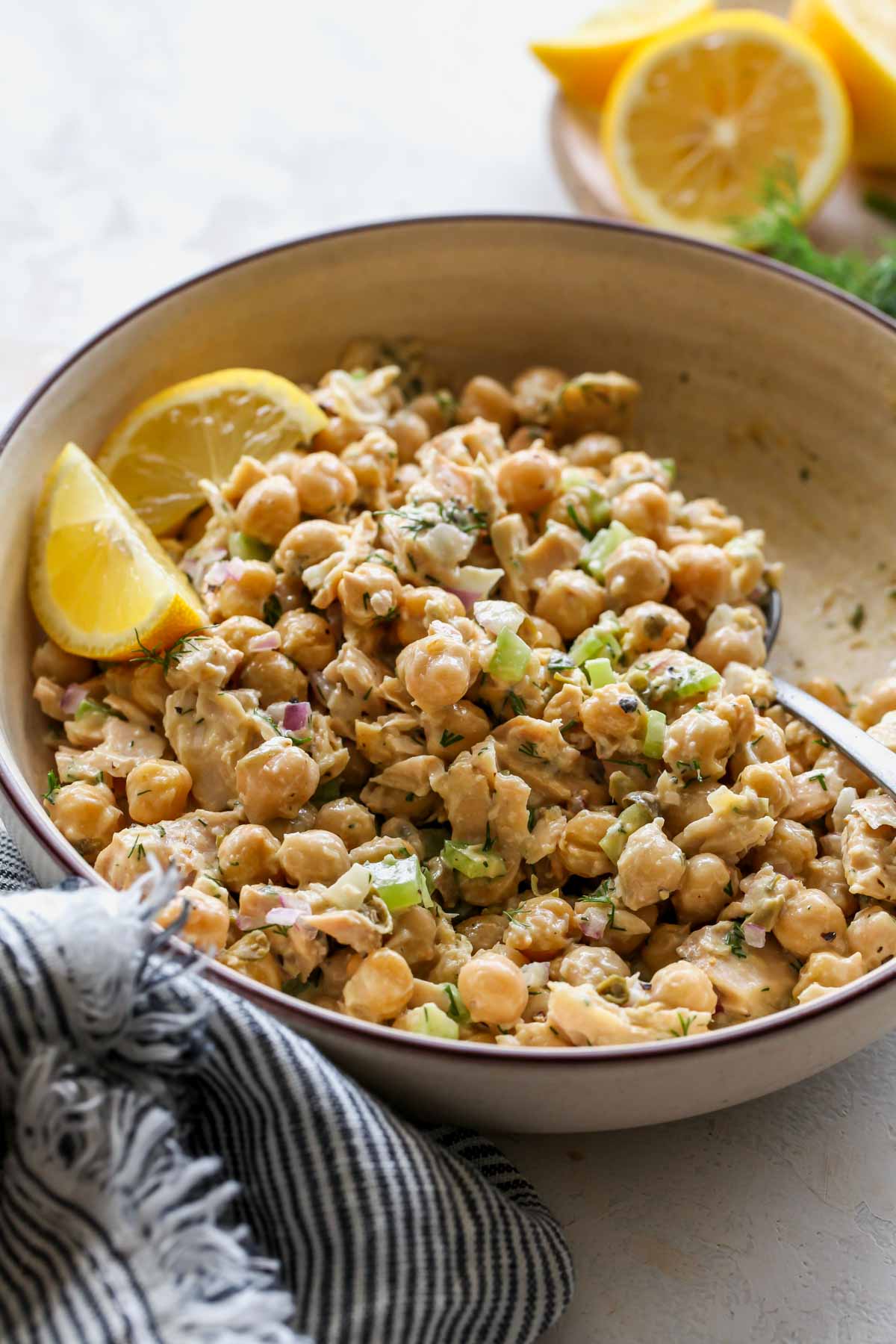 Chickpea tuna salad being stirred in a bowl. Lemon wedges on the upper left side.