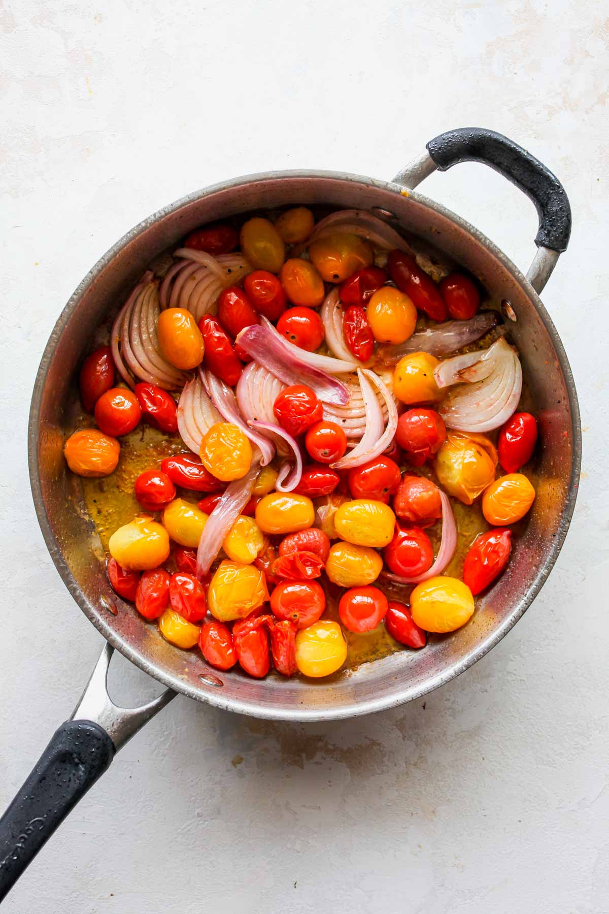 Cherry tomatoes and onions sautéing in a skillet
