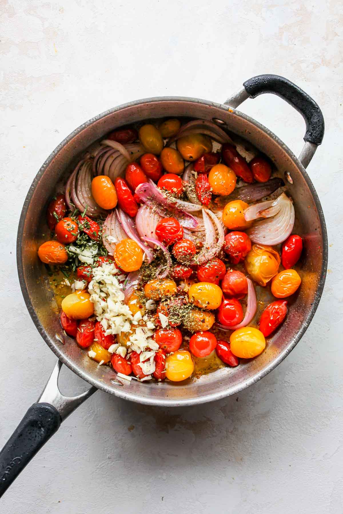 Garlic and spices being added to a skillet of tomatoes