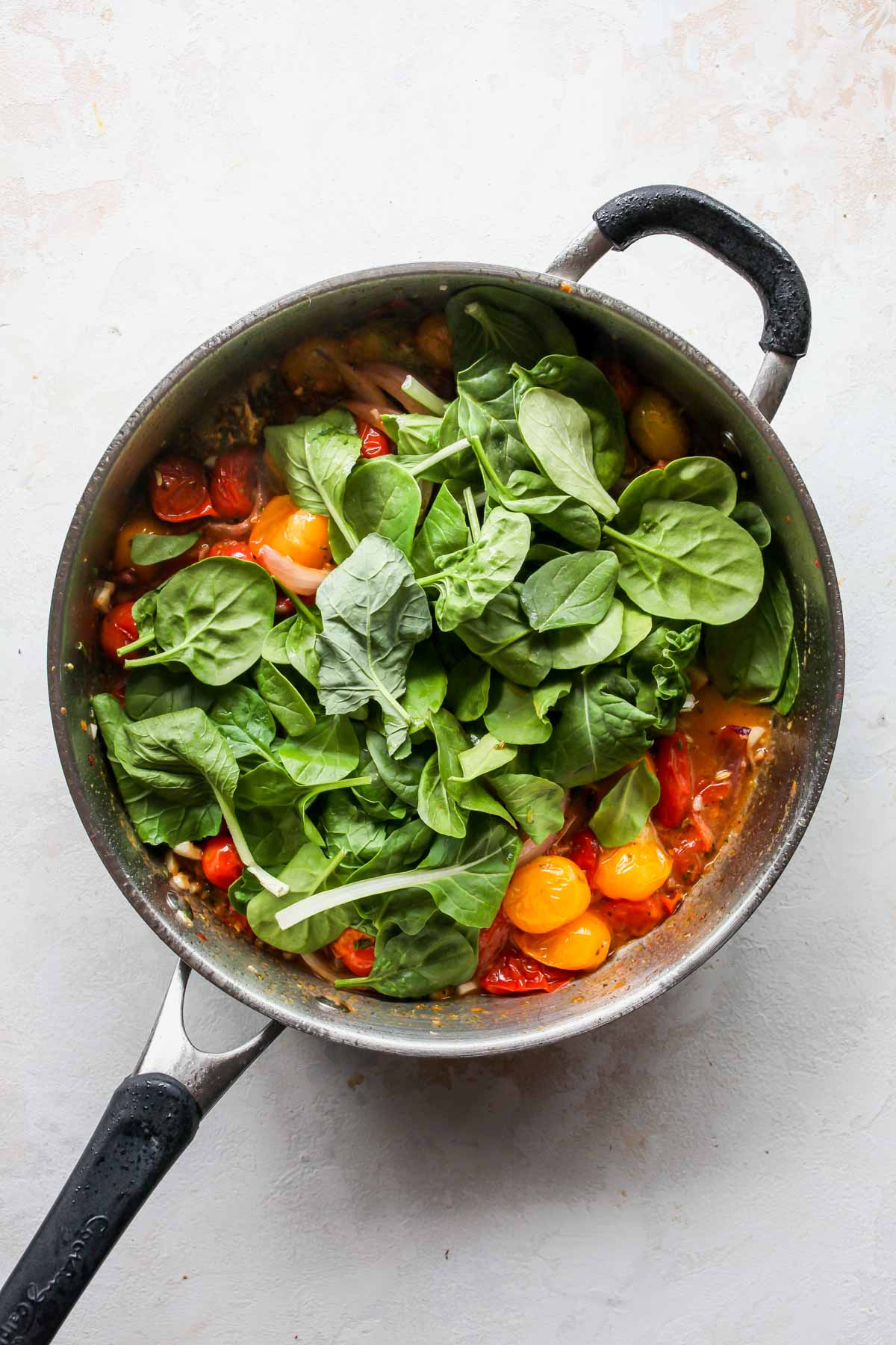 Spinach being stirred into a pan of sautéed vegetables