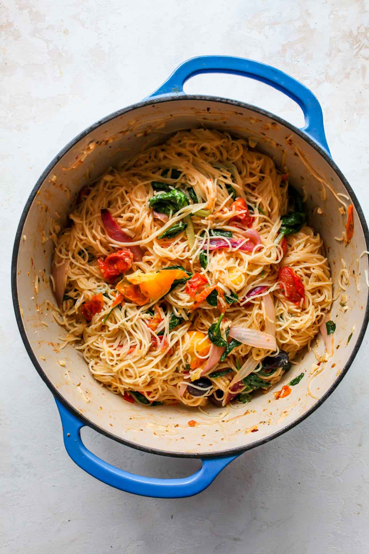 Finished pasta being tossed together in a blue Dutch oven