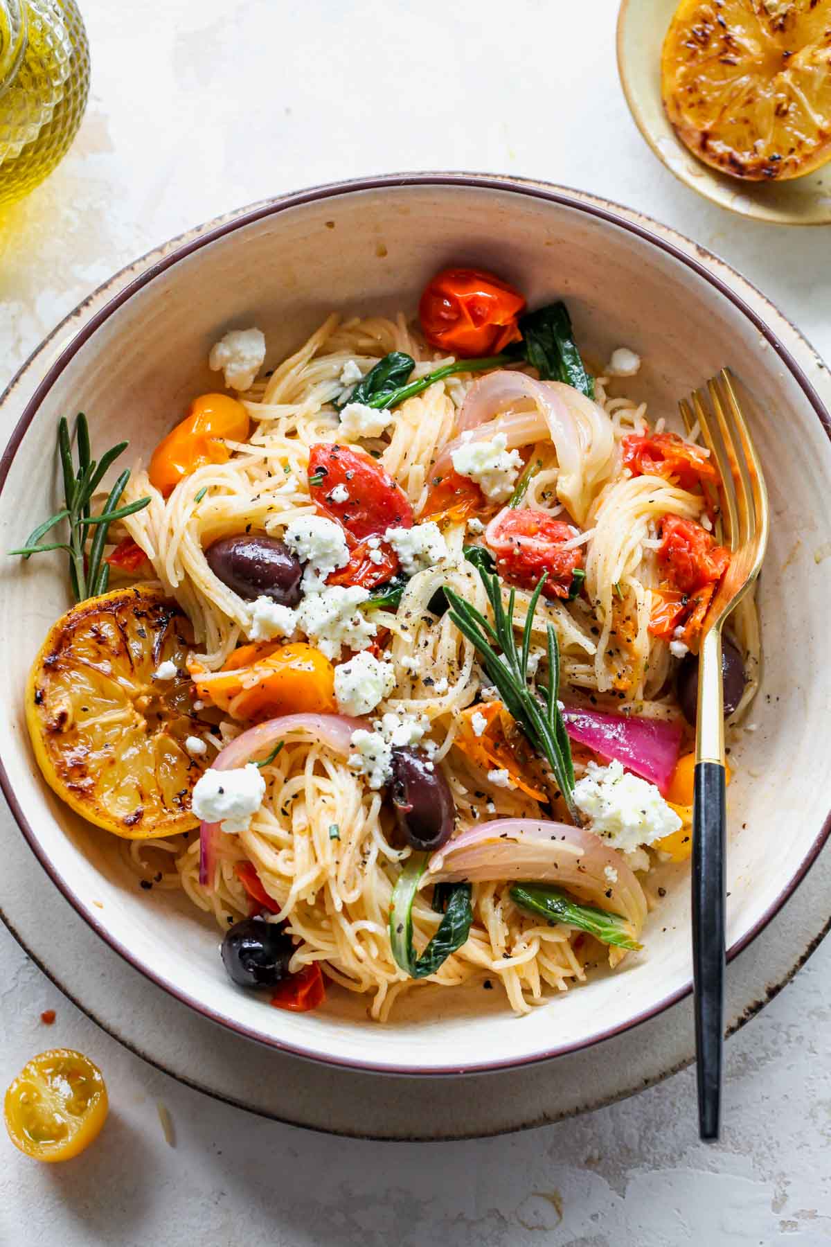 Mediterranean spaghetti in a tan bowl topped with olives and feta cheese