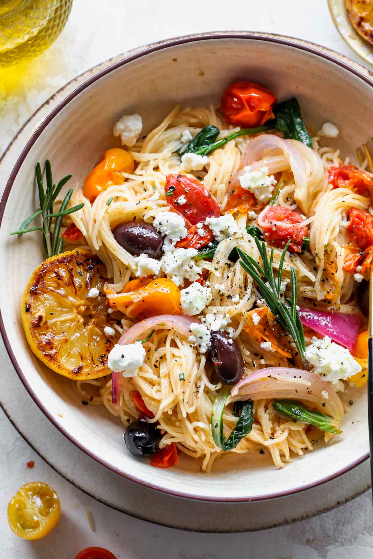 Angel hair spaghetti in a bowl with cherry tomatoes, rosemary, and olives.