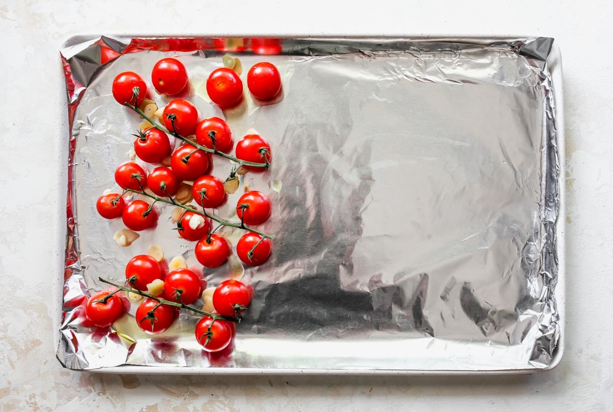 Cherry tomatoes coated in olive oil on a sheet pan