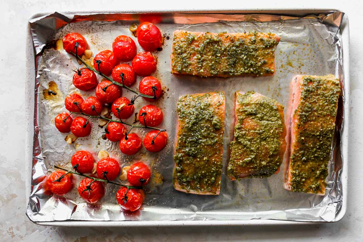 Salmon and tomatoes being roasted on rimmed baking sheet