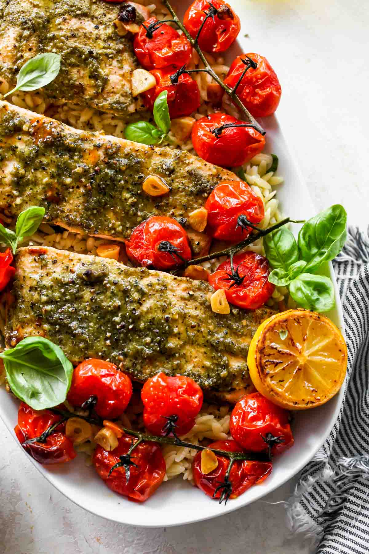 A white platter filled with roasted tomato orzo topped with pesto salmon and lemon