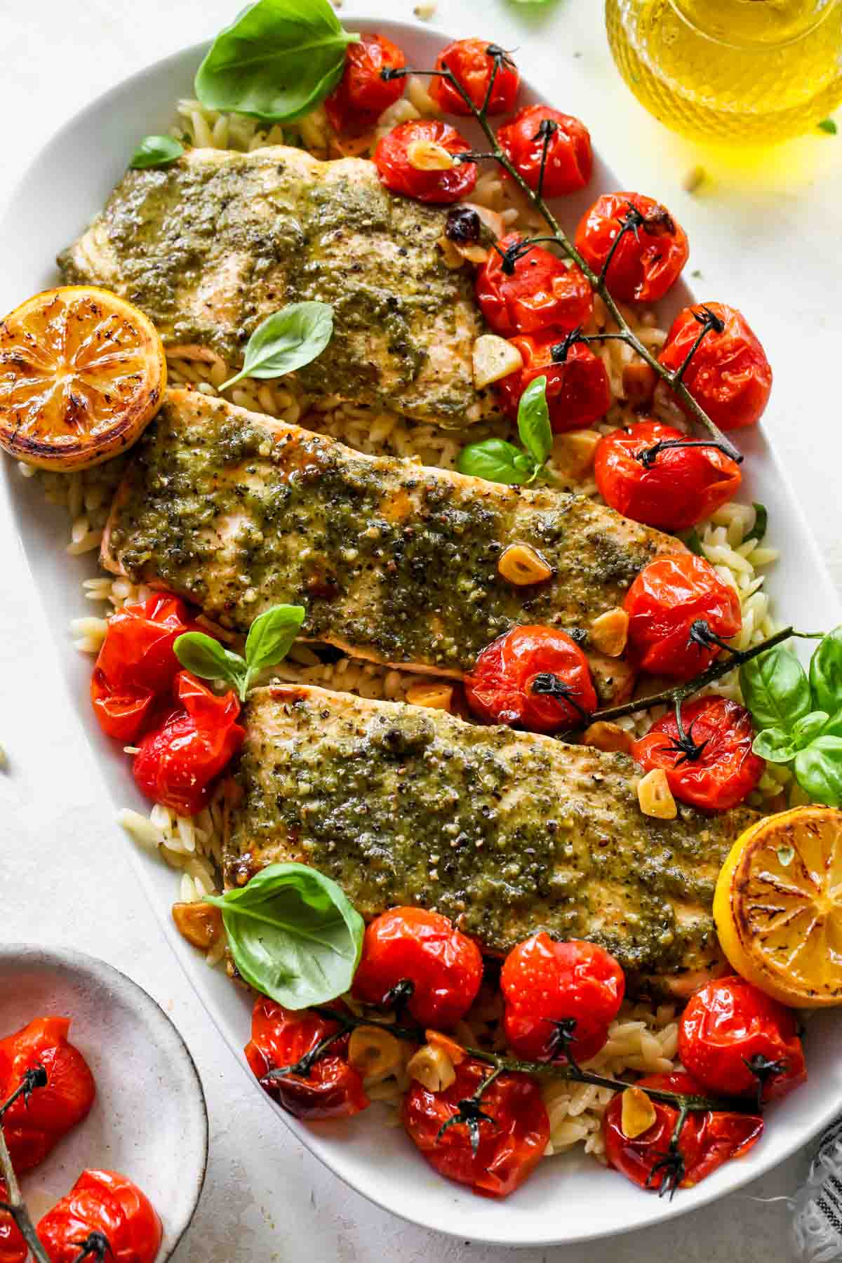A platter of roasted tomato orzo topped with pesto salmon