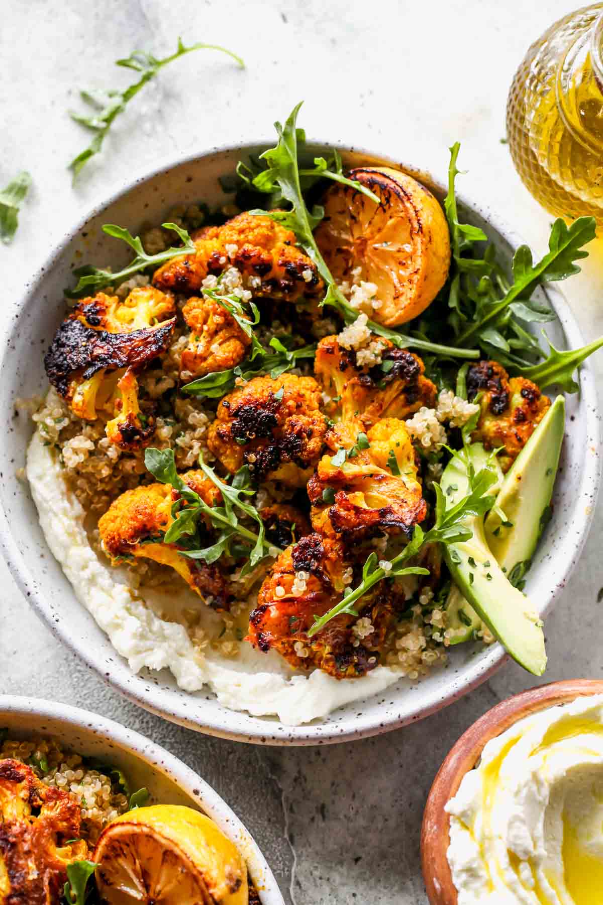 Whipped feta in a bowl topped with roasted cauliflower, quinoa, arugula, and avocado slices.