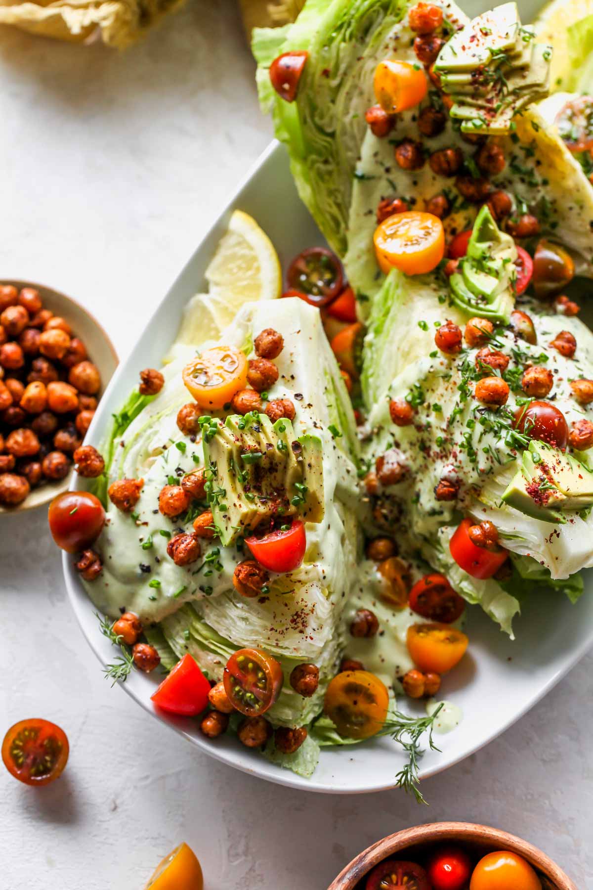 Wedge salad on a platter topped with tomatoes, avocado, and herbs.