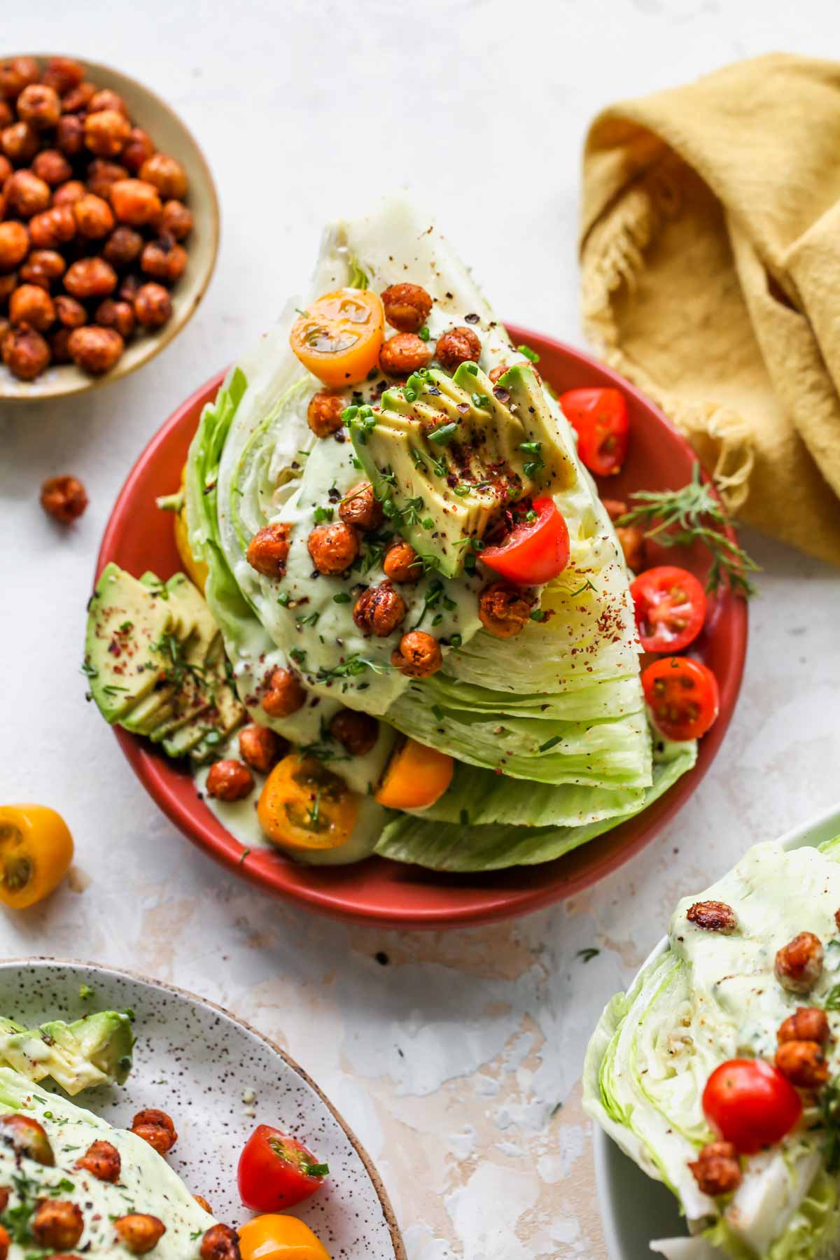 Iceberg salads on separate plates topped with dressing, chickpeas, tomatoes and herbs